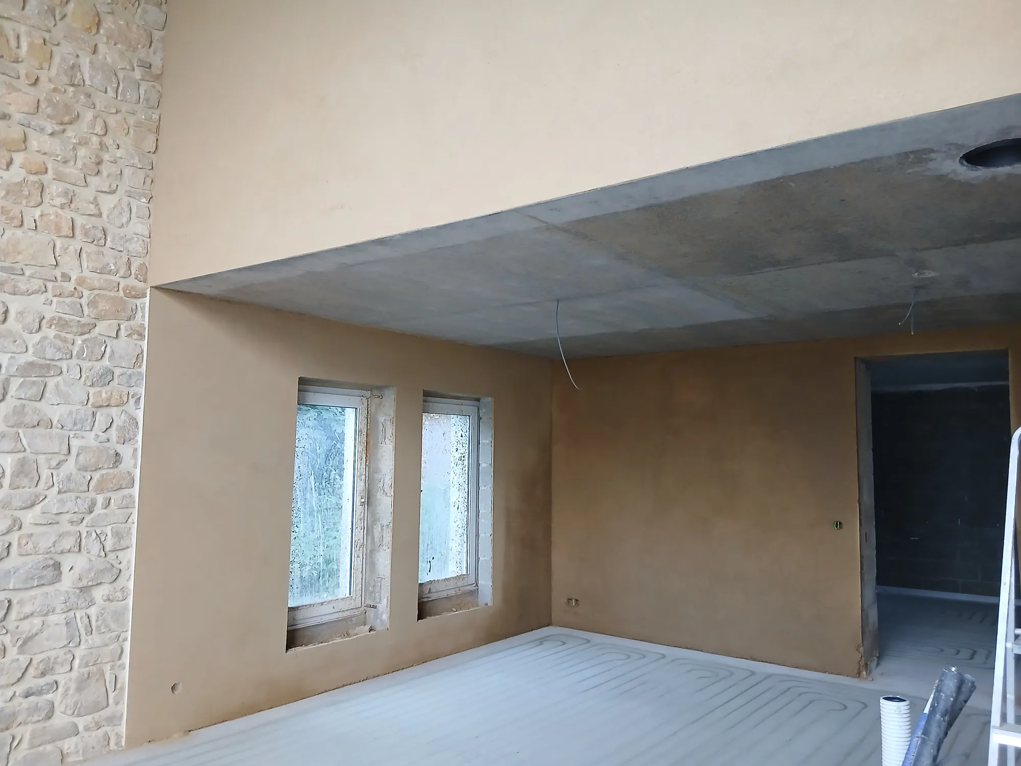 Séjour d'une maison en pierre enduit à l'argile, poutres apparentes et grande baie vitrée