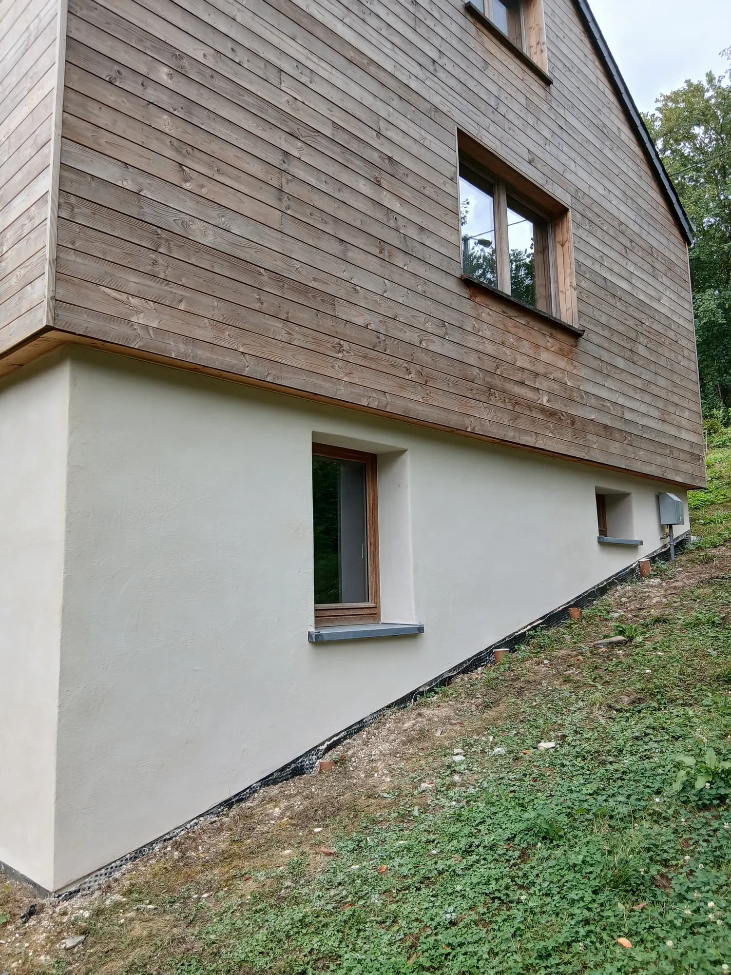Maison contemporaine à bardage bois dont le soubassement est enduit à la chaux teinte sable