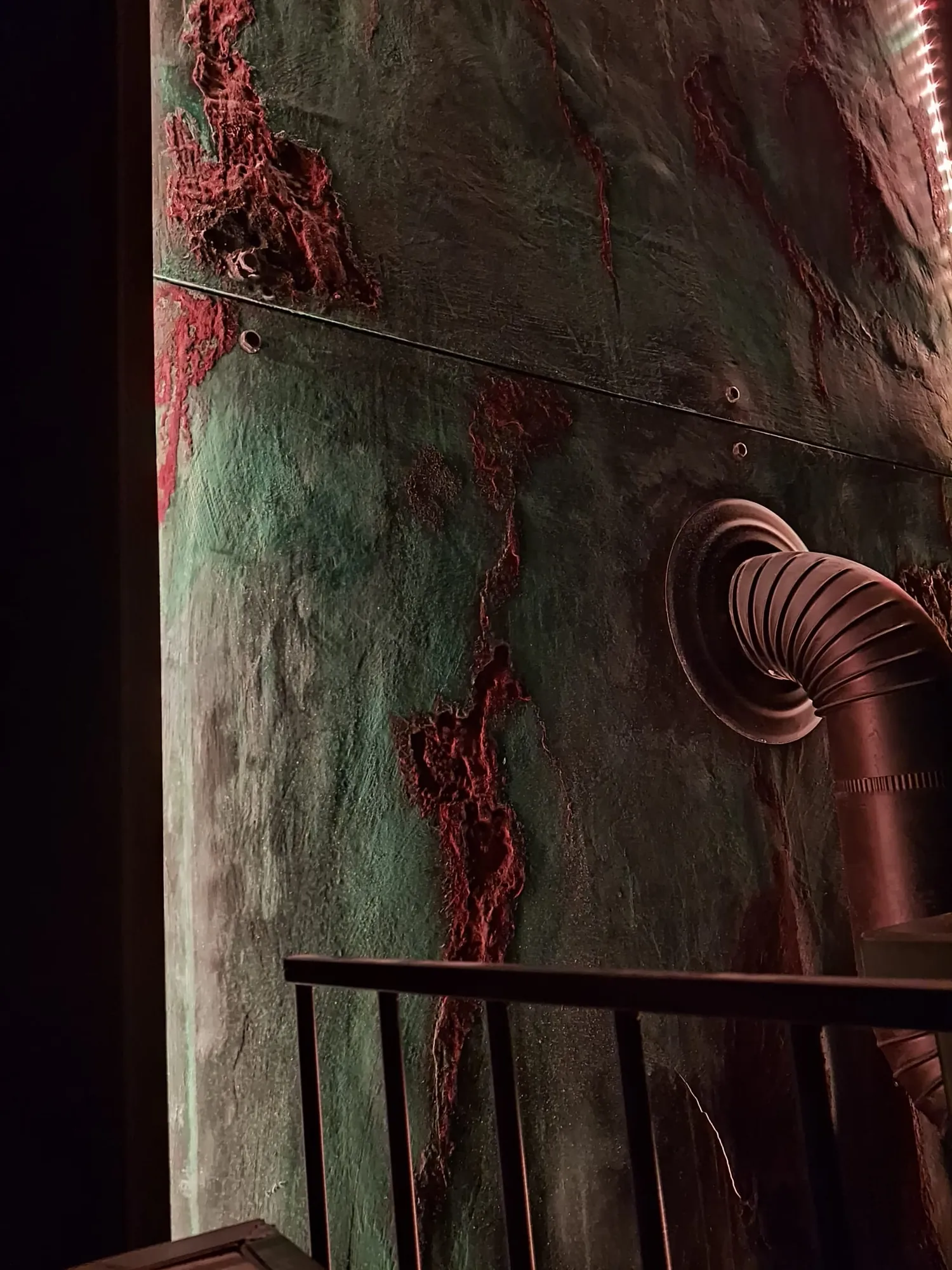 Mur décoratif en enduit à effet métal oxydé, nuances rouille et vert-de-gris, le long d'un escalier