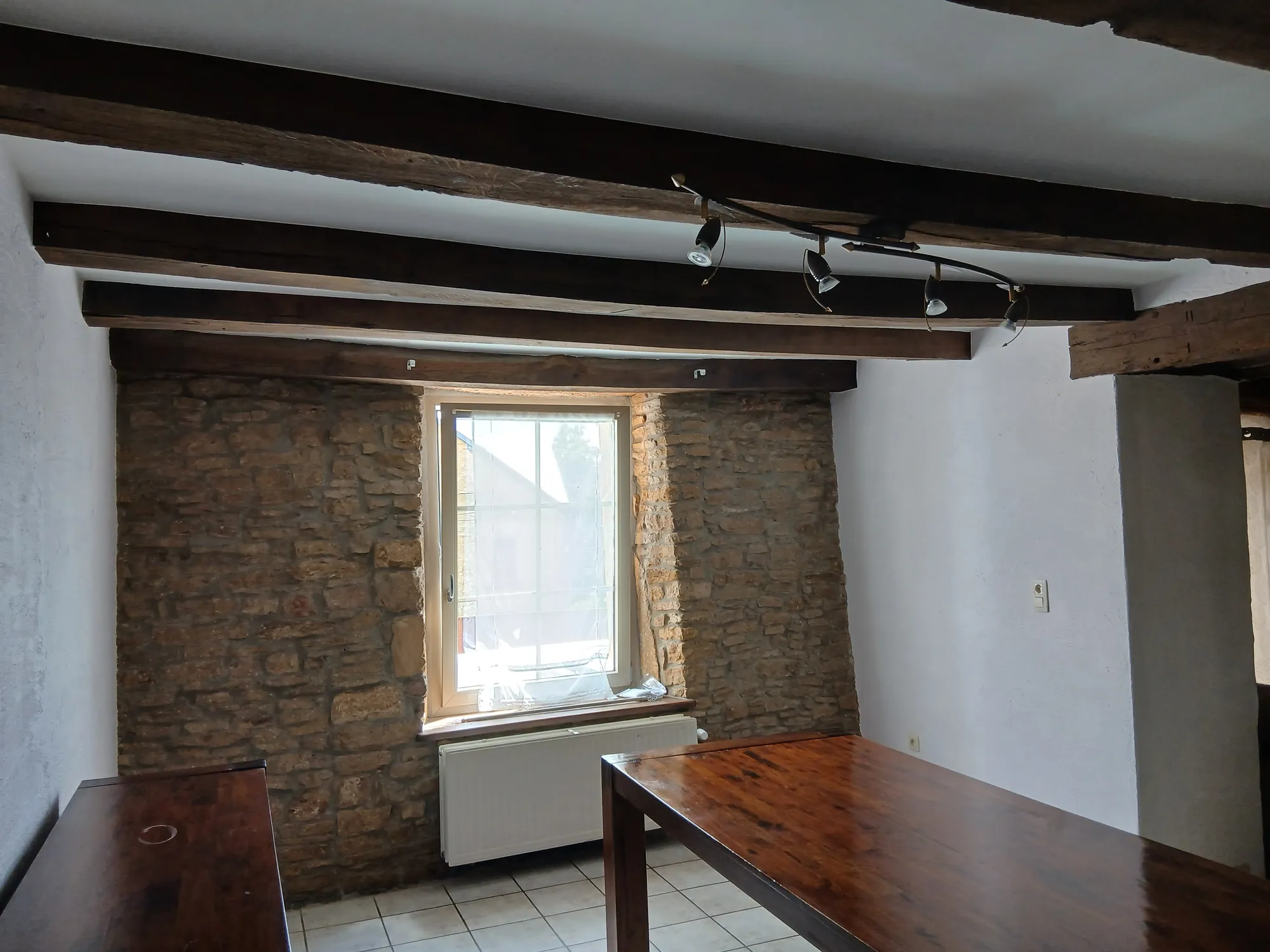 Salle à manger d'une maison ancienne aux poutres apparentes et murs blancs mats